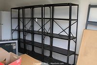 Four black metal shelving units next to refrigerator and wall, fully and partially assembled, showing size and overall condition.