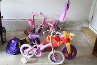 Photo showing two pink and purple Disney Princess themed bikes, red and yellow lion face tricycle, pink and purple scooter, and two purple pop-up crawl tunnels with a purple storage bag
