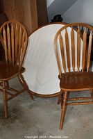 Two wooden chairs and a pedestal table top with a ceramic tile surface showing a crack