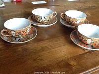Four Japanese porcelain tea cups and matching saucers arranged on a wooden table, showing overall set and design detail