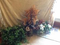 Photo showing all three faux flower arrangements together: green philodendron leaves in a basket, pheasant feathers in tall vase, and hydrangea flowers in vase.