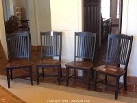 Front view of four wooden chairs lined up, painted black, with wooden seats and slatted backs.