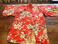 Full view of child's traditional Japanese kimono in red with colorful figures and floral patterns laid flat on table.