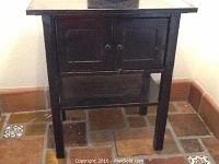 Front view of black painted side table showing cabinet doors with knobs and lower shelf.