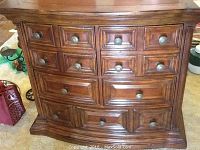 Front view of medium brown finished wood dresser with five drawers and decorative paneling.