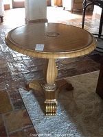 Front angle view of the round wooden table highlighting the medallion on the tabletop and base design.
