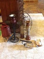 Photo showing various candle holders including metal sconces, ceramic candle holders, and a glass lantern-style holder on a carpeted floor