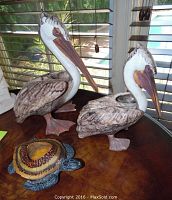 Two ceramic pelican figurines and a ceramic turtle candle holder shown on table near window with blinds