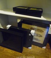 Three black shadow boxes stacked on a shelf, unopened in packaging, along with black picture frames below.