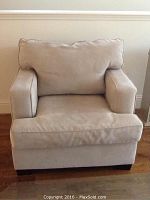 Front view of oversized tan upholstered chair showing cushion shapes and armrests.