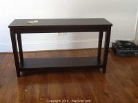 Full front view of wooden sofa table with dark finish, showing rectangular top and bottom shelf, standing on wood floor by white wall.