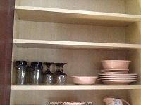Shelved pink Fiestaware ceramic items including stacked plates and bowls.