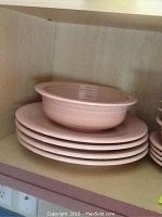 Four peach/light pink bowls stacked on dinner plates on shelf