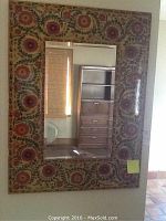 Full view of the mirror hung on a wall, showing the frame pattern and reflected room contents.