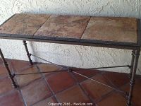 Photo of metal frame console table with a top made of three large ceramic tiles in rustic earth tones with detailed metal legs and crossbars.
