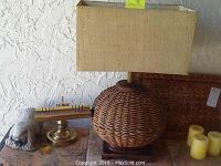 Photo showing woven rope lamp with beige rectangular shade, stone rabbit figurine, brass item, and 4 pillar candles on stone surface