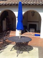 Full view of round wrought iron table on patio with blue umbrella raised