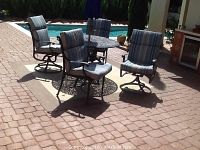 Four wrought iron chairs with striped cushions arranged around a circular wrought iron table on a brick patio near a pool