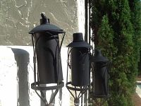Overall view of the four black metal tiki torches of varying sizes, showing design and condition outdoors.