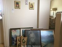 Framed artworks leaning against wall including large winter landscape, grayscale portrait, and smaller paintings