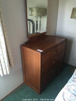 Photo showing the dresser with attached mirror against wall near window and bed.