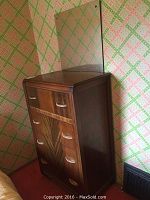 Vintage dresser with patterned wood drawer fronts, showing wear, and attached mirror.