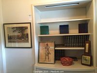 Overall display of framed prints, basket, encyclopedias and barometer on white shelving unit