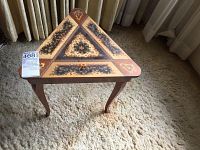 Full view of triangular wooden table with intricate floral inlay pattern on the top and curved legs, placed on carpet.
