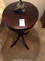Photo of the round top of the wooden side table with a small decorative item on it, showing dark wood finish and smooth surface.