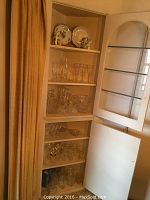 Photo of cabinet with multiple shelves displaying clear crystal glassware, crystal decanter, ice bucket, pitcher, and several small bowls.