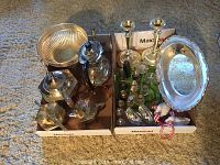 Overall lot of silverplated tea and coffee pots, creamer, sugar bowls, salt and pepper shakers, candlesticks, and trays arranged together in boxes on floor.