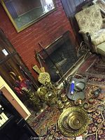 Wide view showing various brass fireplace accessories arranged near a brick fireplace, including the blower, umbrella stand, brass plates, lanterns, and fireplace tools grouped on an oriental rug.