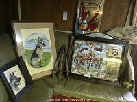 Overview photo showing two framed German Shepherd paintings, Jardin de Paris mirrored sign, and Lorne Whisky mirrored advertising sign on a bench with an easel.