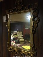 Large ornate wood framed mirror with carved decorative elements and beveled glass, showing reflection of room and furniture.