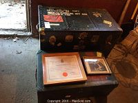 Two vintage military trunks stacked, with framed certificate and photo on top, showing markings, labels, and military stenciling.