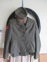 Olive drab women's US Marine Corps dress jacket and matching cap displayed hanging together, showing external condition and style with sleeve patch.