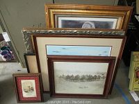 Group photo of six framed prints and vintage signs stacked against a wall, varying frame styles and sizes, some wear visible