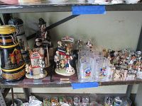 Shelf displaying two decorative ale bottles and several Flambro Day at the Fair ceramic figurines with carnival scenes, alongside four Disney character-themed drinking glasses and multiple small dog figurines.