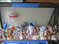 Top shelf photo showing a collection of miniature Disney figurines, a lidded cut glass candy dish with red band, ceramic mugs, and various small animal figurines including dogs and others.