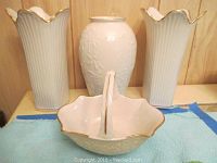 Two tall fluted white vases with gold rims and one white embossed floral vase plus a white porcelain basket with gold trim.