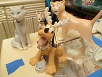 Photo showing three Disney Lenox Aristocats cat figurines and Pluto figurine with reindeer antlers accessory on table.