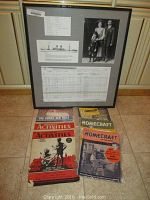 Framed immigration ship manifest with family photo and text documents alongside vintage magazines placed on floor