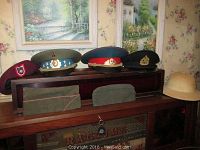 Full view of the collection including six military hats placed on a wooden cabinet and a safari hat to the right