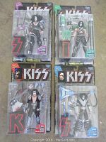 Four unopened KISS action figures in original packaging, each with accessories, showing front view of packaging and figure detail.