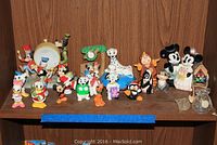 Multiple small Disney character figurines displayed on a shelf, including Mickey Mouse, Minnie Mouse, Pluto, Bambi, 101 Dalmatians characters, Donald Duck, Daisy Duck, and others in various poses and colors.