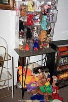 Front view of a collection of Beanie Babies in clear protective cases arranged on a small table with several loose stuffed animals including Underdog at the table base.