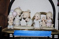 Four figurines displayed on a shelf, including three Precious Moments figurines and one Enesco figurine.