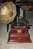 Full view of gramophone on carpeted floor showing wood base, horn, and record platter