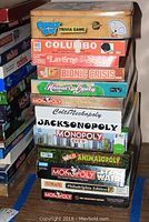 Stack of 13 assorted board games including Family Guy Trivia, Columbo, Laverne & Shirley, Monopoly variations such as Colts Neckopoly and Jacksonopoly