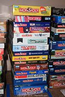 Stacked view of Monopoly board games including Philadelphia, New York, Century 21 Opoly, Simpsons, SpongeBob, Harley Davidson editions